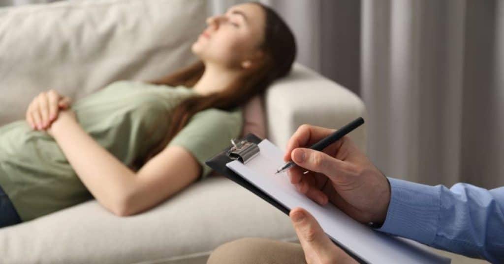 Een cliënte ligt met gesloten ogen bij haar therapeut of psycholoog op de bank tijdens een sessie hypnotherapie.