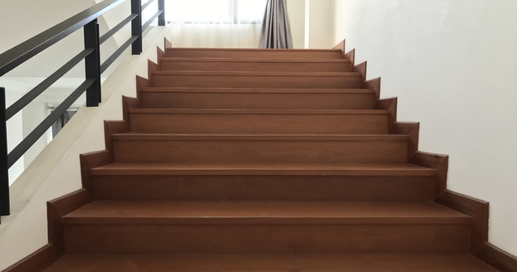 Een brede trap in donker hout: de treden en de plinten zijn in dezelfde donkere kleur. De zwarte trapleuning is van metaal.