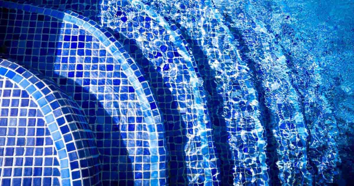Een ingebouwde trap in een zwembad met helder water. De trap is afgewerkt met blauwe mozaïektegels.