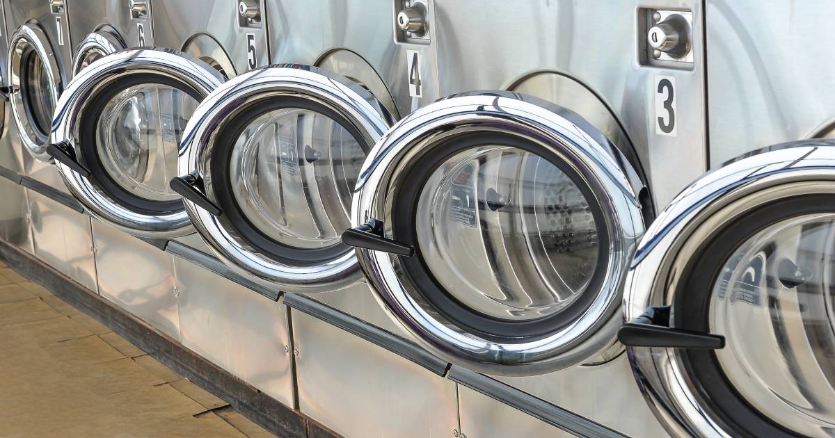 Beeld uit een wasserij: een rij met 5 industriële wasmachines met geopende deuren.