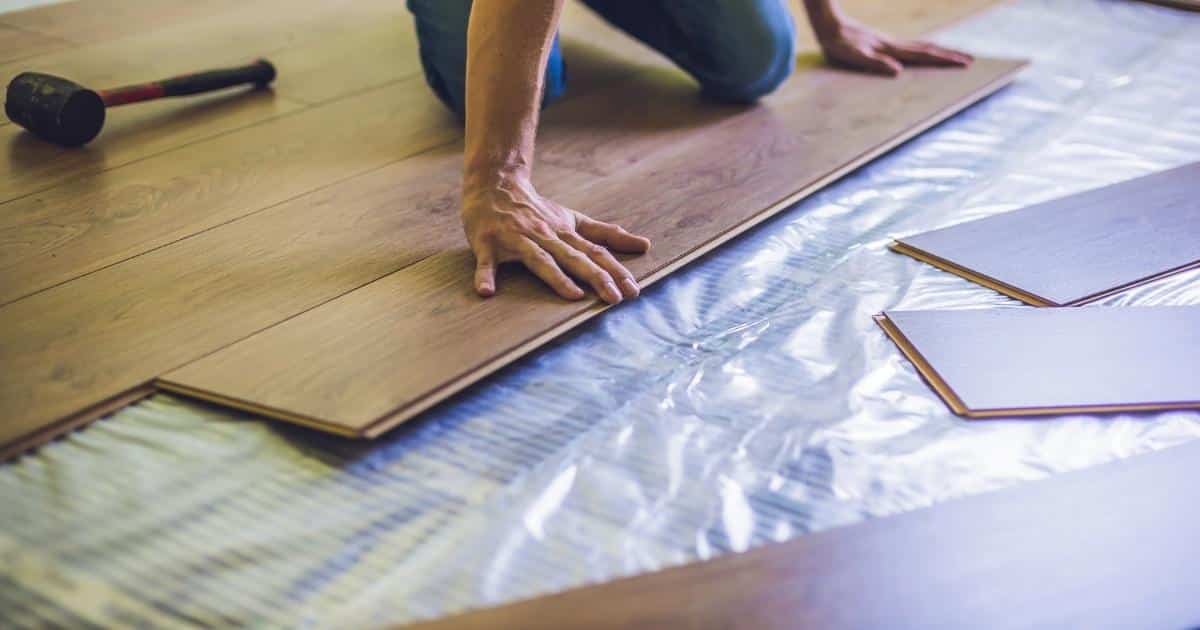 Een installateur plaatst laminaatparket op een vloer met een folie voor infrarood vloerverwarming.