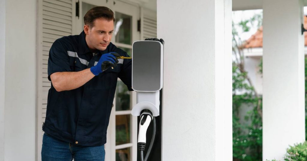 Een installateur van laadpalen aan het werk met de plaatsing van een klassieke laadpaal of laadzuil tegen de witte gevel van een woning.