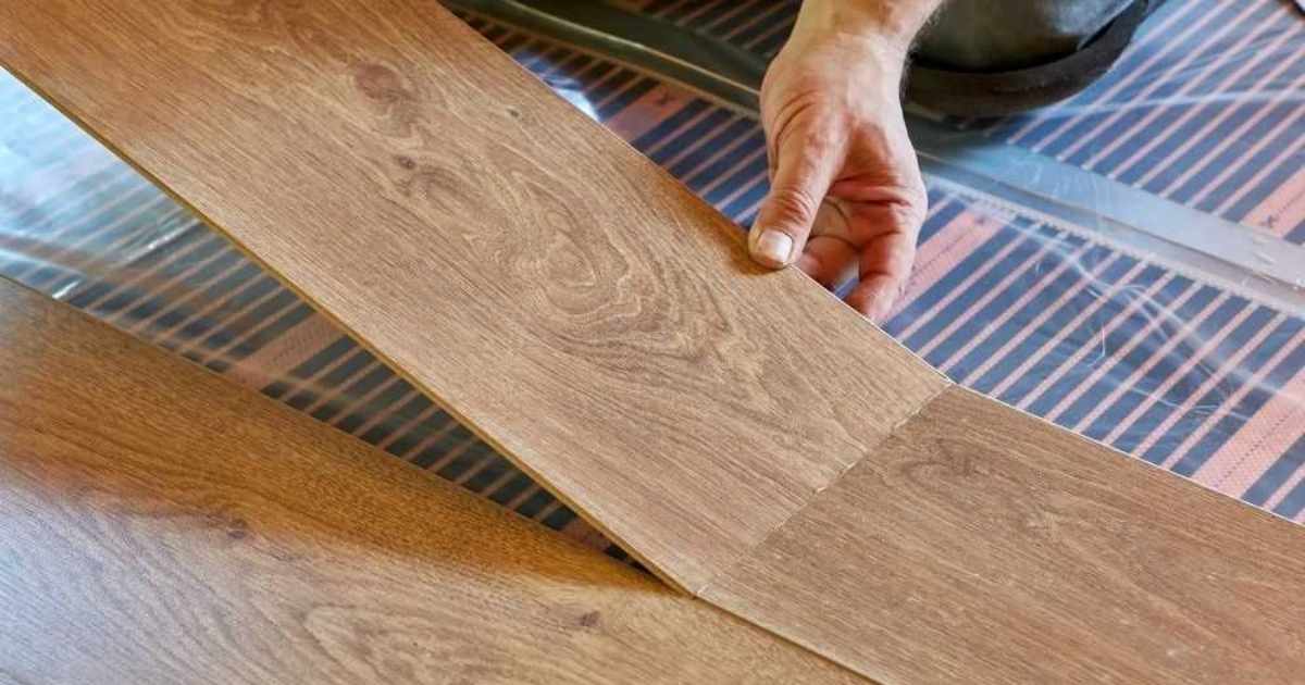 Een installateur legt houten laminaat parket over een vloer met infrarood vloerverwarming.