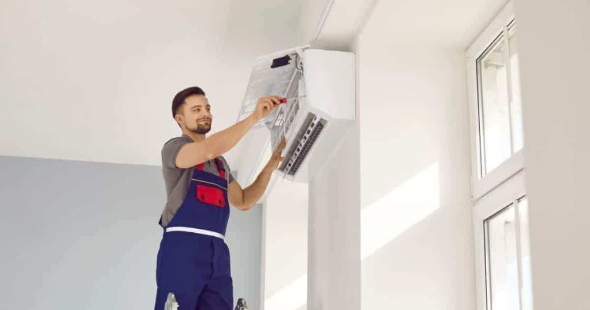 Installateur met blauw werkpak die een airconditioning binnenunit installeert aan het plafond in een woning.