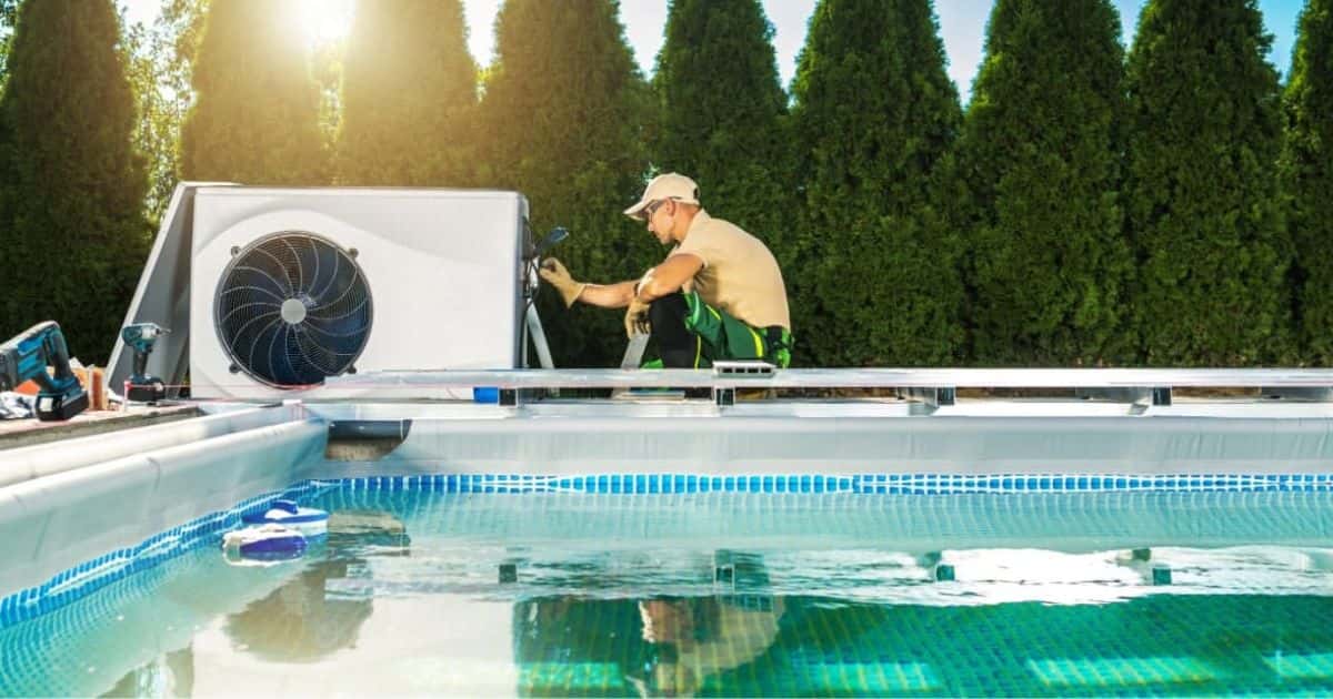 Een monteur van een warmtepomp met lichtbruine pet en polo sleutelt aan een warmtepomp unit bij een zwembad met helder water.