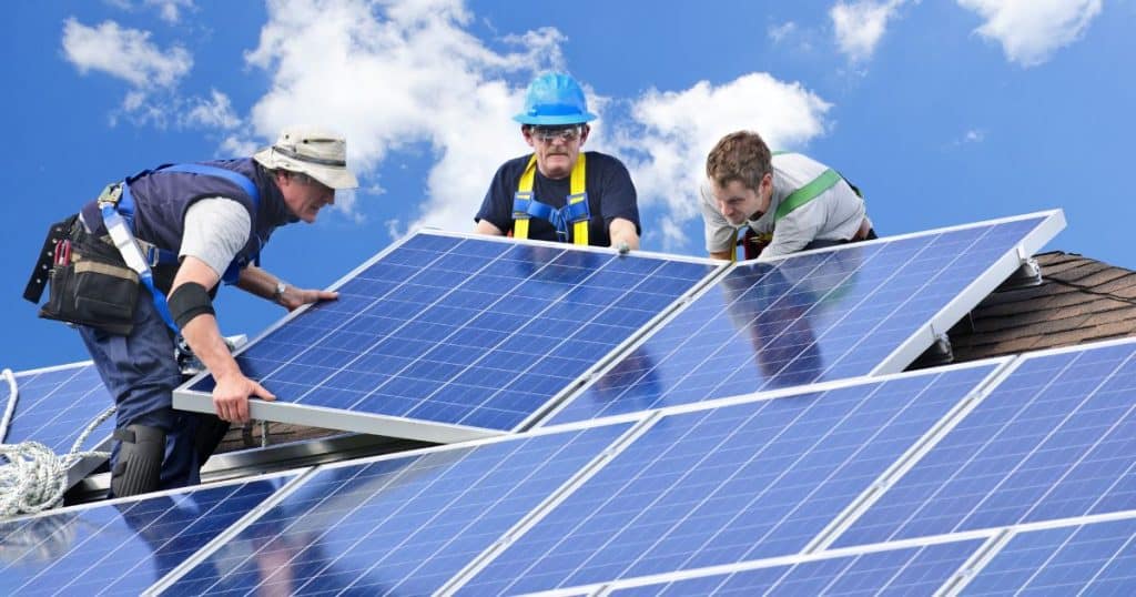 Drie installateurs plaatsen blauwe zonnepanelen op het dak van een woning.