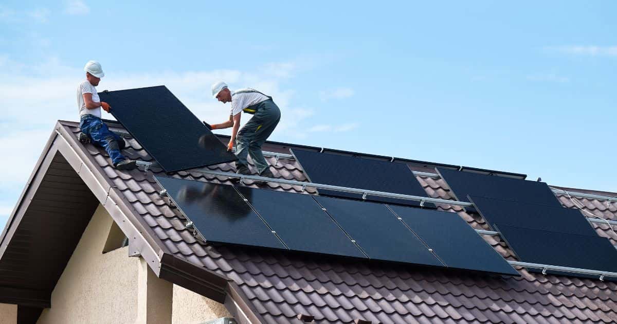 Twee vakmannen zijn bezig met het installeren van zonnepanelen op een schuin dak op een huis in Aalst