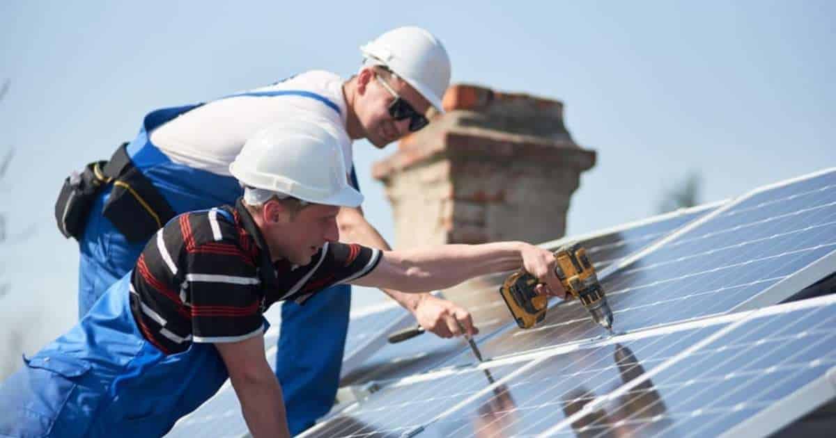Installatie Zonnepanelen door 2 vakmannen in blauwe overall en witte helm.
