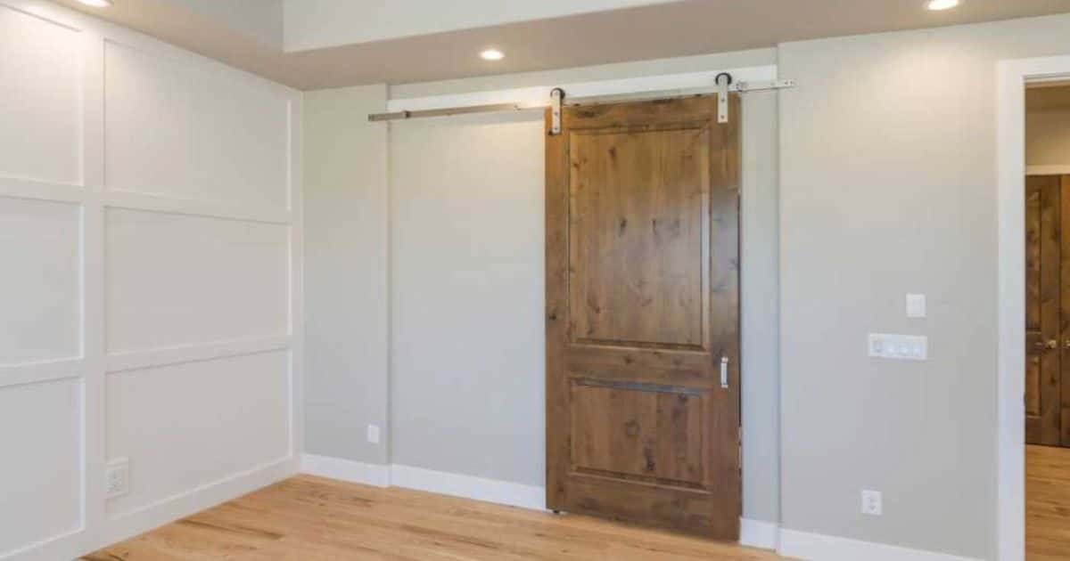 Houten hangende schuifdeur in kamer, met spots in het plafond, beige geverfde muren en witte houten wand.