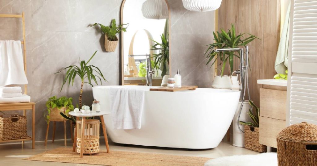 Een badkamer met een natuurlijke uitstraling, een wit bad met ronde hoeken, een losstaande kraan, een spiegel en verschillende kamerplanten.