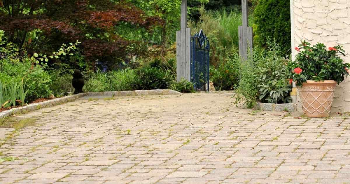 Een oprit met tegels in verschillende formaten. De oprit geeft uit op een klein blauw poortje. 