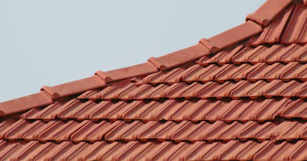 Zijaanzicht van de nok van een pannendak met keramische dakpannen en nokvorsten in klassieke oranje tint.