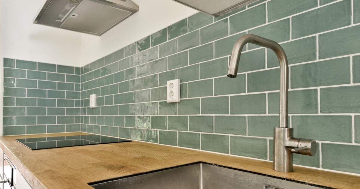 Een betegelde spatwand in een keuken, afgewerkt met lange groene tegels in halfsteensverband. Onder de spatwand ligt een houten aanrecht, met ingebouwde kookplaat en lavabo.