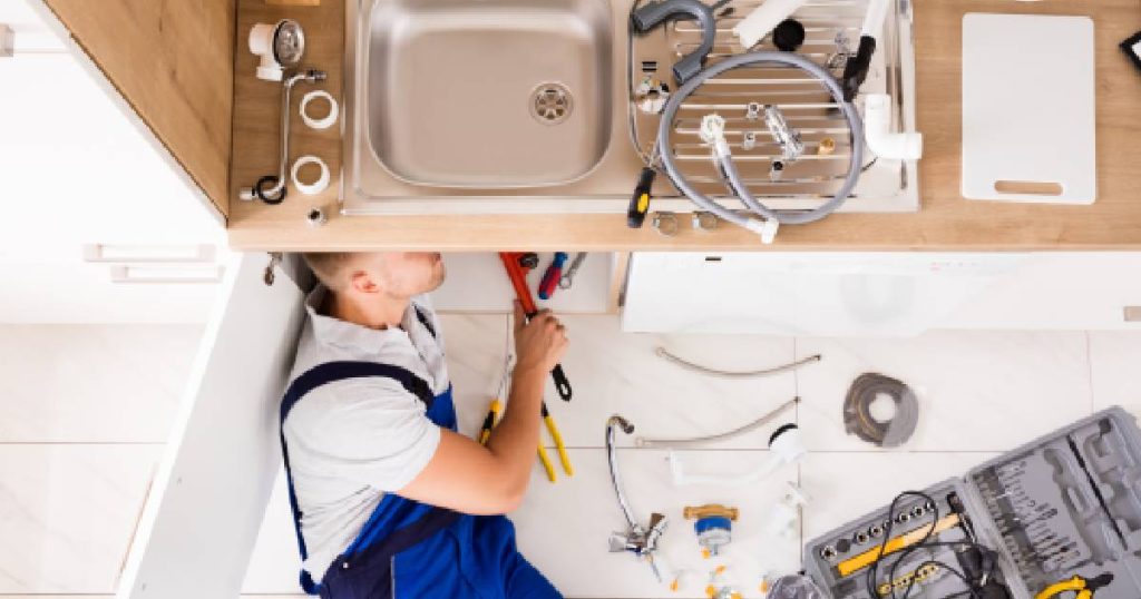 Een loodgieter werkt aan de leidingen in een keuken.