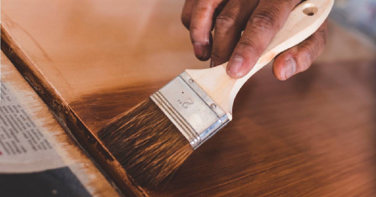 Iemand schildert een houten oppervlak met een schilderkwast.