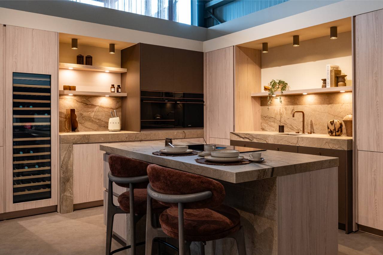 Luxe moderne keuken van Keukens De Abdij met een natuurstenen kookeiland, licht houten kasten en een ingebouwde wijnklimaatkast.