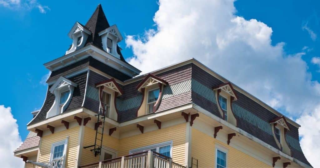 Onderaanzicht van een klassieke woning met mansardedak en torentje tegen een heldere blauwe lucht met witte wolken.