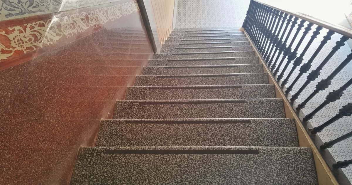Een klassieke siergrind trap met antislip en een houten trapleuning aan de rechterkant. De muur links is bekleed met marmer.