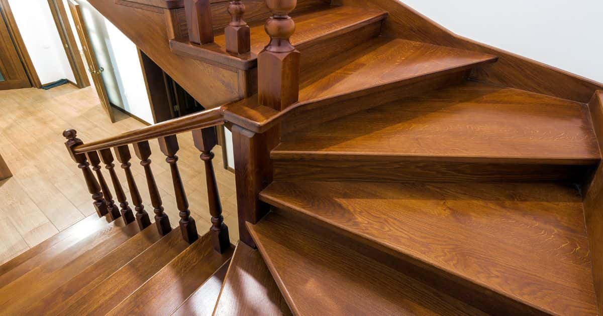 Een klassieke trap in donker hout die uitkomt op een lager gelegen verdiep met laminaat- of parketvloer. 