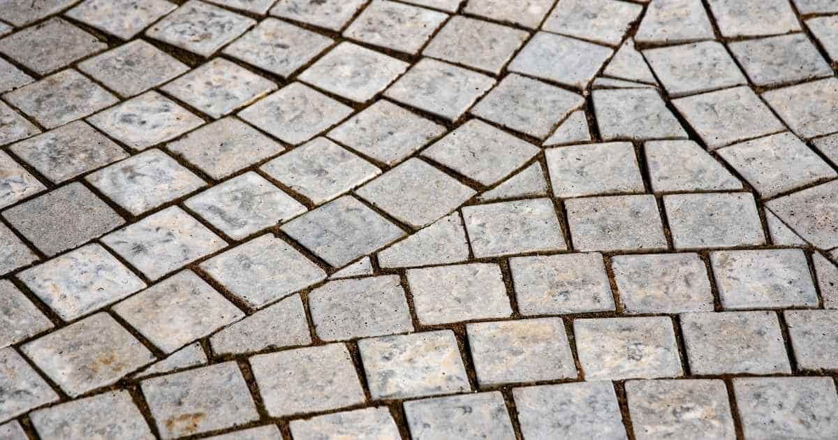 Kleine, grijze tegels op de vloer van een terras. De tegels vormen bogen die elkaar raken.