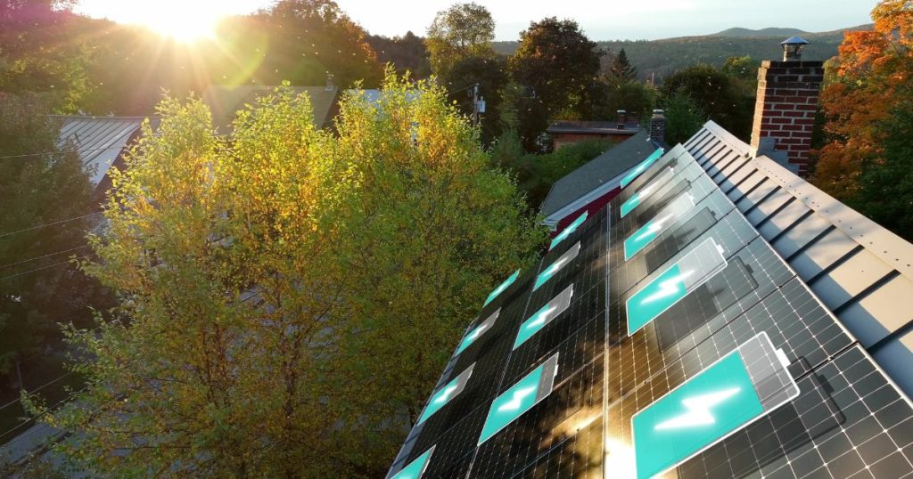 Een dak met zonnepanelen waarop batterijen afgebeeld staan. Elke batterij is tot een ander percentage opgeladen. De woning staat in een groene omgeving.