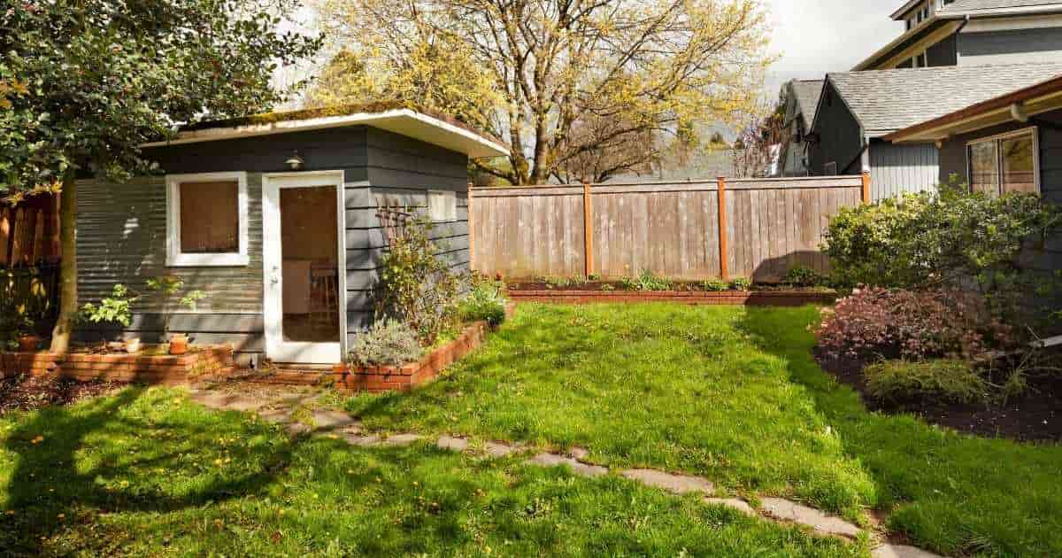 Een klassieke tuin met houten omheining, tuinhuisje en een smal pad van stapstenen.