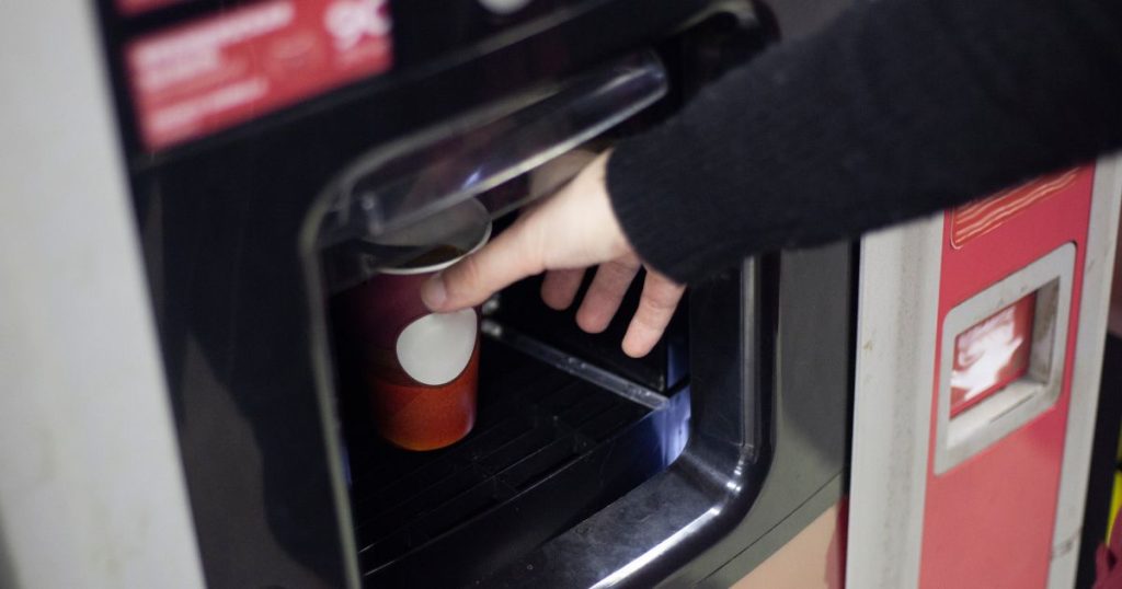Een hand wil een met koffie gevulde beker nemen die in de koffiemachine met muntinworp klaarstaat.