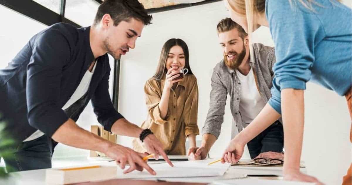 Twee mannen en twee vrouwen staan rond een tafel met papieren. Ze zijn in de weer met het vergelijken van Limburgse sociaal secretariaten. De achterste vrouw drinkt van een doorzichtige tas met thee.