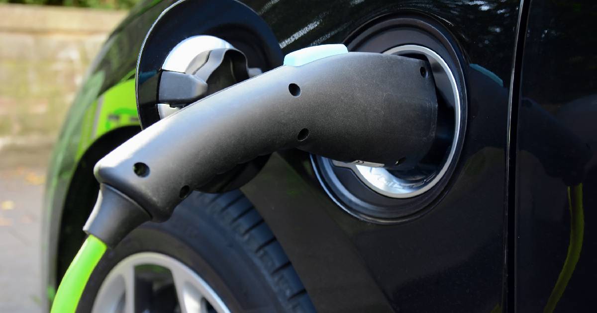 Een zwarte elektrische auto die met een laadkabel is aangesloten op een 3-fase laadpaal bij de eigenaar thuis.