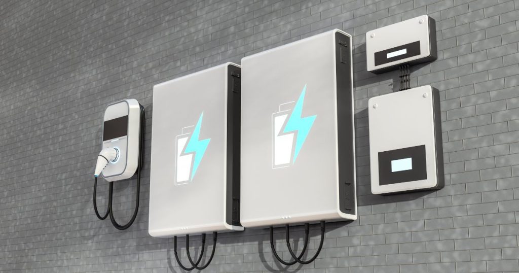 Twee grote thuisbatterijen met een batterij en een blauwe bliksemschicht als logo. De batterijen hangen aan een grijze bakstenen muur.