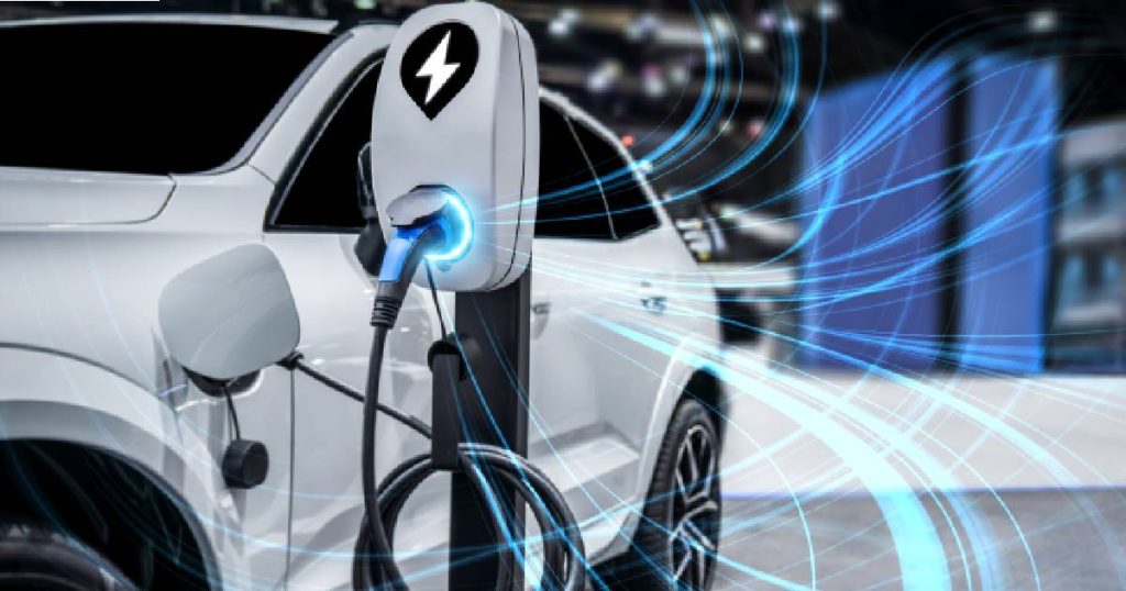 Een witte elektrische wagen laadt op met energie uit een snellaadpaal, een van de laadpalen die een bedrijf ter beschikking stelt op het parkeerterrein bedrijf.