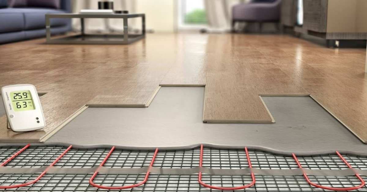 Een woonkamer met laminaat, waaronder een aluminium warmtegeleidingsplaat ligt. Onder de plaat liggen rode buizen voor vloerverwarming, vastgebonden aan een metalen raster. Links op het parket staat een witte thermostaat die een temperatuur van 25,9 graden Celsius weergeeft.