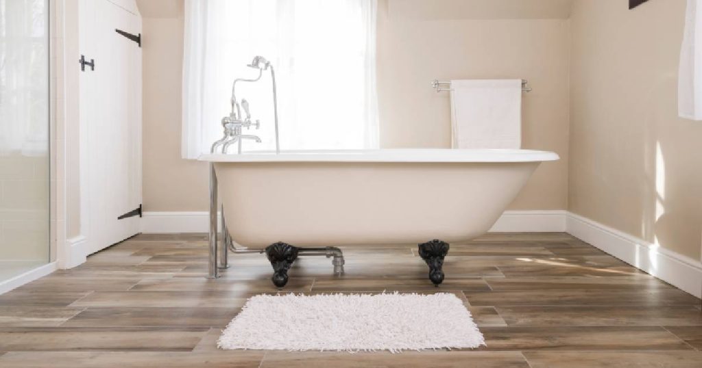 Minimalistische badkamer met meerlaags parket, een wit vrijstaand bad met pluizige witte badmat en lichtroze muren.