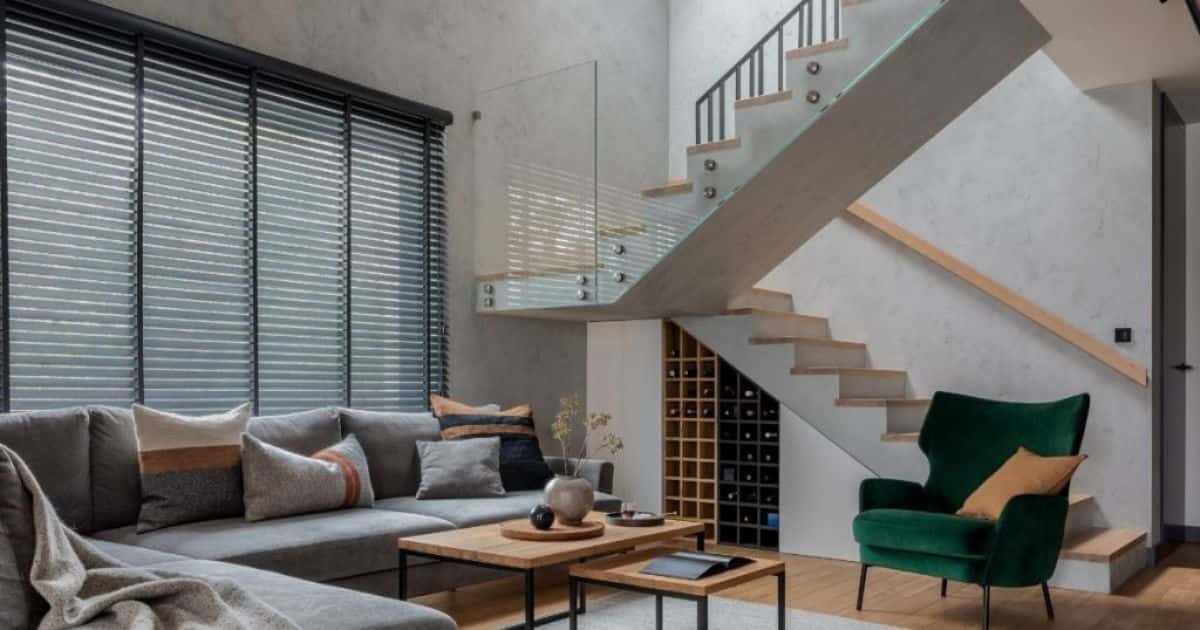 Een lichtgrijze betontrap met houten traptreden in combinatie met een glazen zijwand op het bordes en een trapleuning in hout tegen de gelijkkleurige muur.