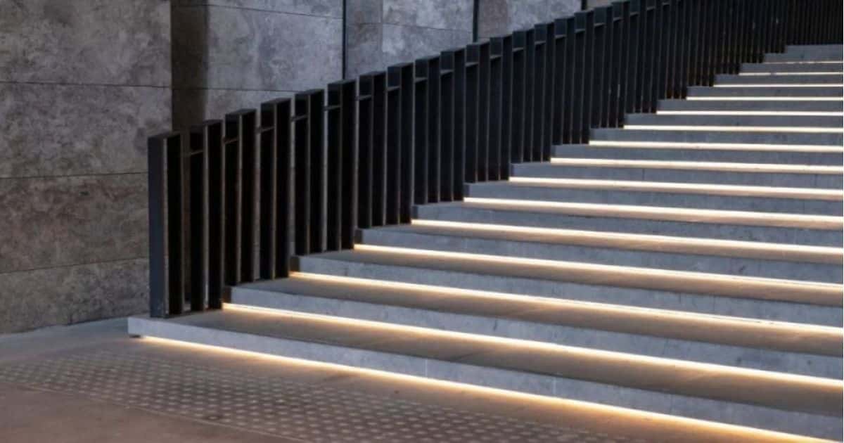 Een luie trap met verlichting onder elke trede en met een zwarte leuning.