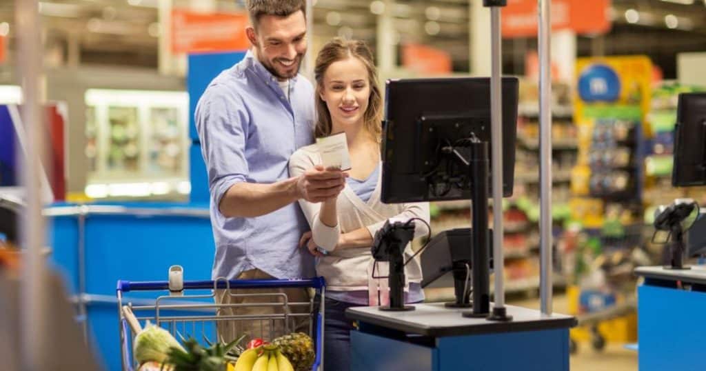 Een man en een vrouw in een supermarkt bekijken de rekening van hun aankopen.