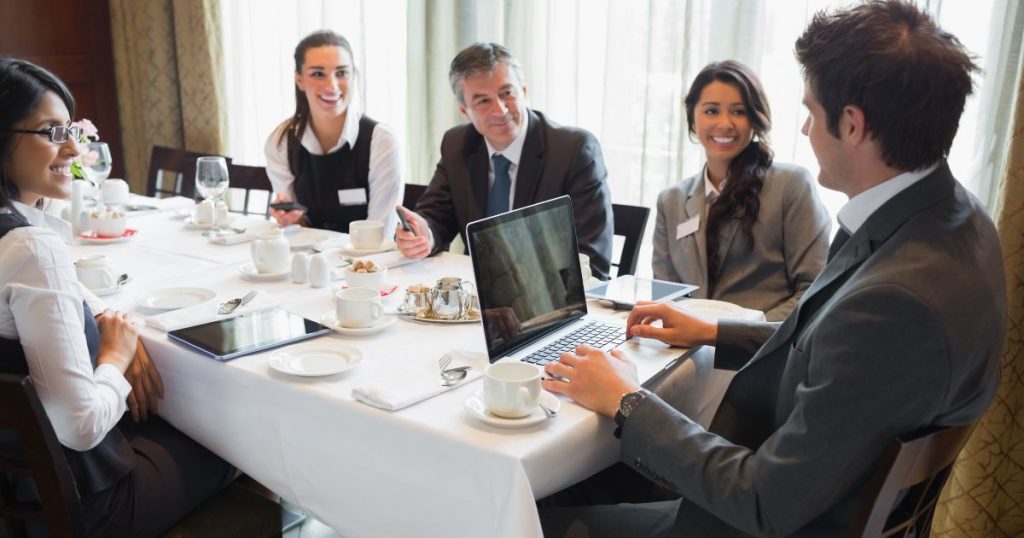 Een groep zelfstandigen en werknemers op restaurant voor een zakelijke lunch. Ze hebben een laptop en tablets bij.