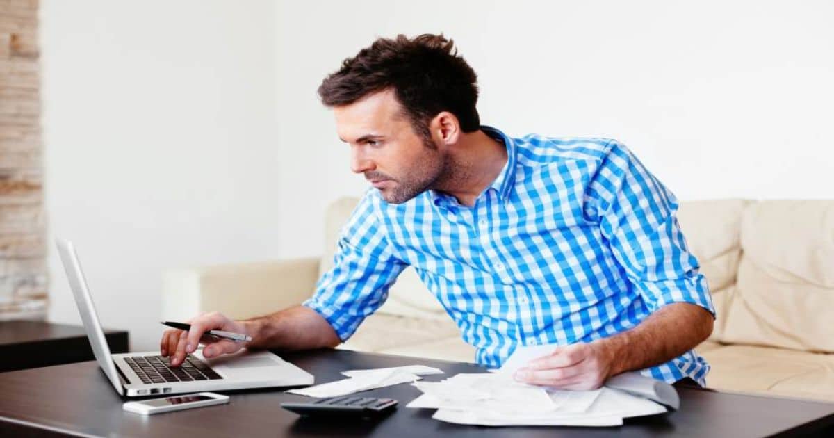 Persoon werkt aan een laptop met documenten op tafel.