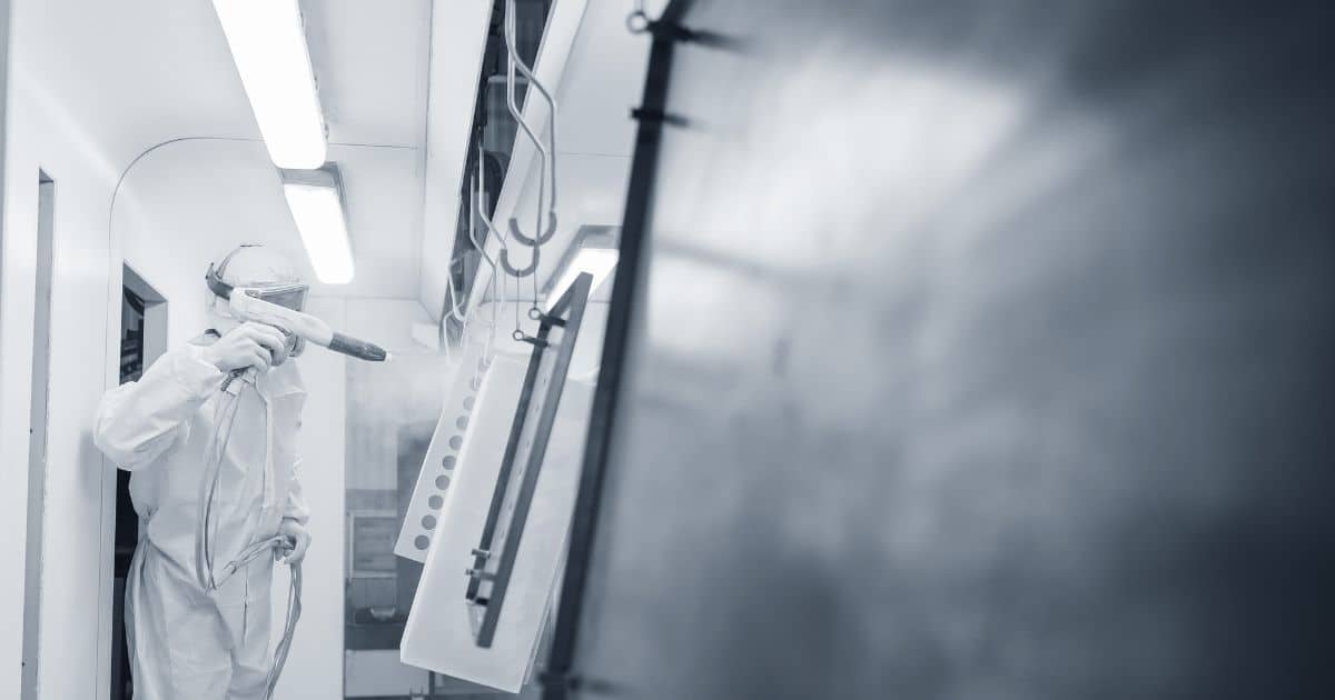 Man in witte, beschermende kledij en met speciale helm om een oppervlak via een speciale spuit te verven.