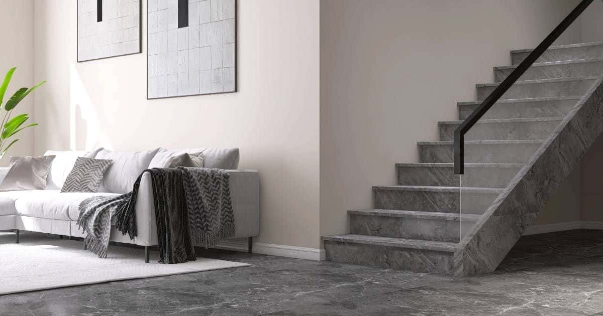 Een trap met afwerking in natuursteen en een glazen trapleuning met zwart metalen rand. De trap loopt onderaan over in een natuurstenen vloer, waardoor de woning een meer uniforme, strakke look krijgt.