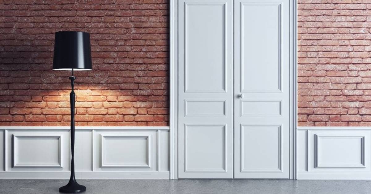 Klassieke, witte en massieve binnendeur in een bakstenen muur naast een zwart lamp. 