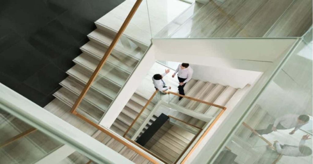 Dubbelkwart trap in kantoorgebrouw. De traptreden zijn van kunststof (laminaat, pvc, HPL ...). De trapleuning is een combinatie van glas met een houten handgreep.