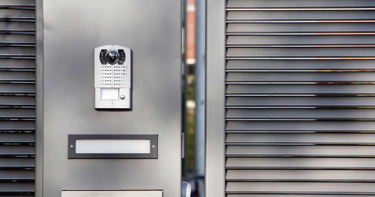 Een intercom aan een grijze metalen poort op een oprit.