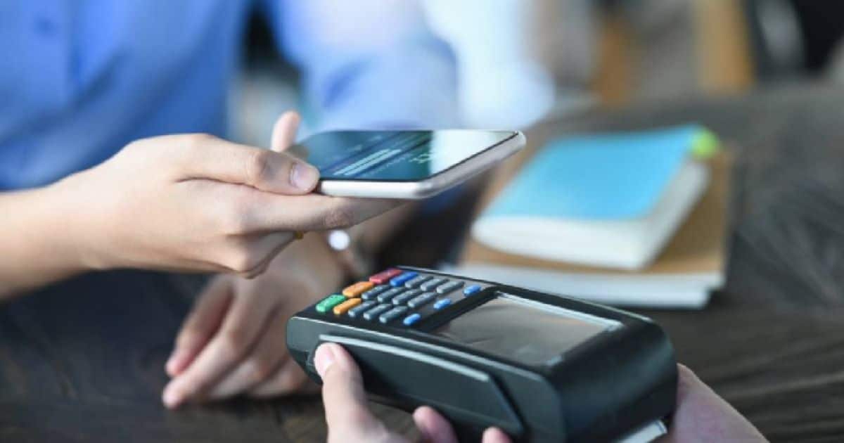 Klant houdt een smartphone boven een mobiele betaalterminal om contactloos te betalen, terwijl de winkelier het toestel vasthoudt.