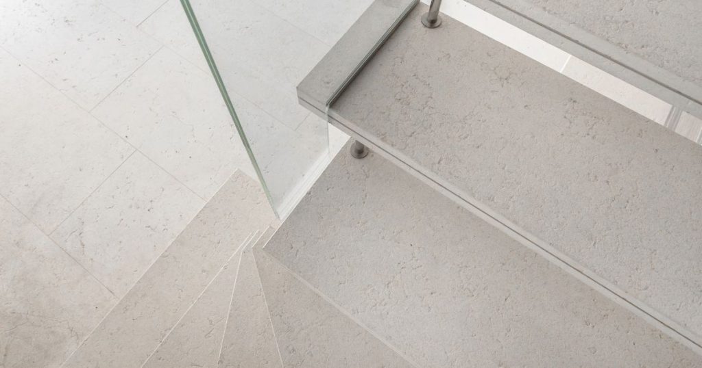 Een open trap met overzettreden in lichte betonlook en glazen trapleuning.