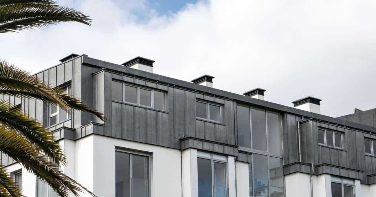 Een modern gebouw met plat zinken dak. De zinken dakbedekking loopt mooi over in zinken gevelbekleding, die het bovenste deel van de gevel bedekt. De onderste helft is bedekt met witte gevelpleister. 