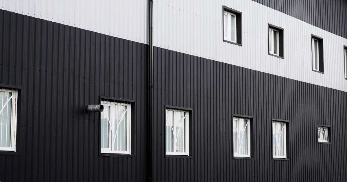 Gevel van een modern gebouw, afgewerkt met zwarte en witte sandwichpanelen. De panelen werden aangebracht in witte en zwarte stroken. Elk paneel is afgewerkt met een trapeziumprofiel met smalle banen.