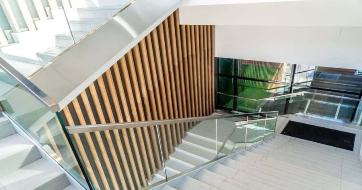Moderne trap met verticale houten latten als lambrisering en een glazen balustrade met metalen trapleuning.