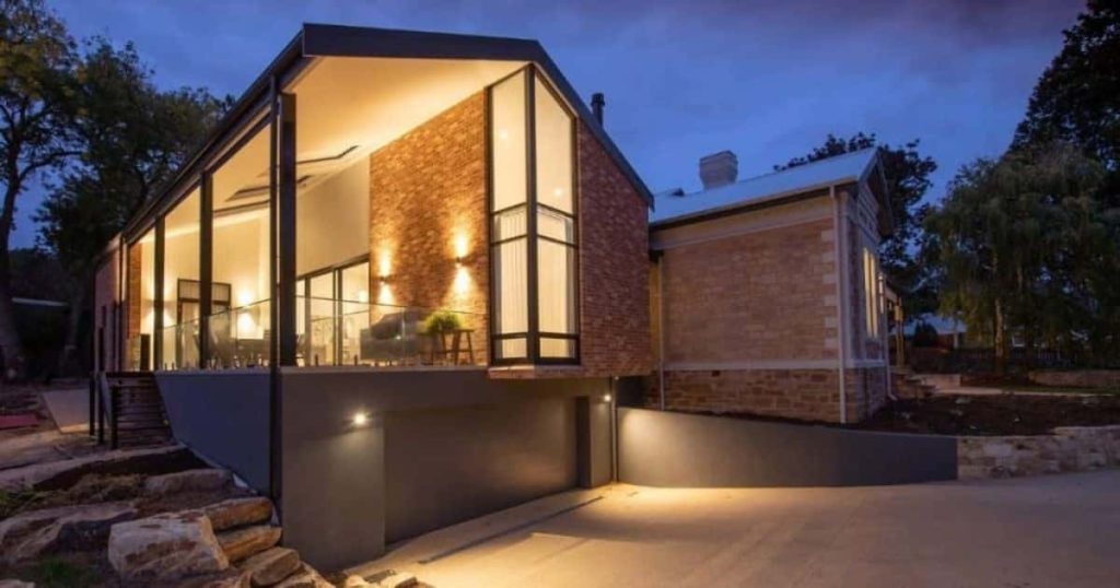 Buitenkant van een bakstenen woning waaraan een bakstenen uitbouw werd geplaatst. De woning beschikt voorts over een ruim overdekt terras en een ondergrondse garage met hellende oprit.