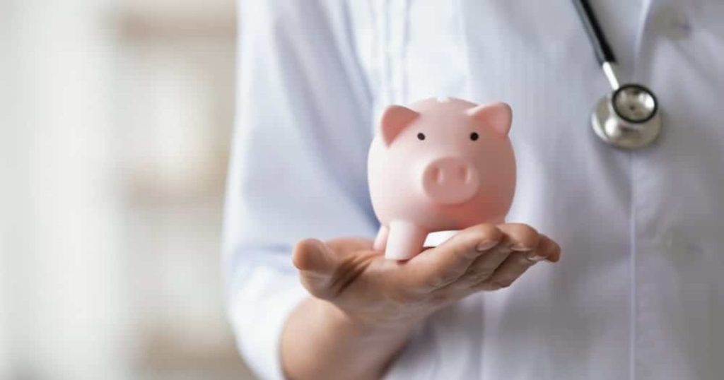 Wat kost de overstap naar een andere mutualiteit? - Een dokter houdt een roze spaarvarken in zijn hand.